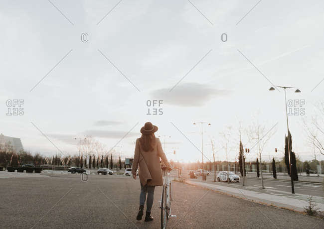 Young hipster woman going with a bicycle during sunset