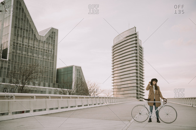 Young hipster woman with a bicycle on bridge in the city