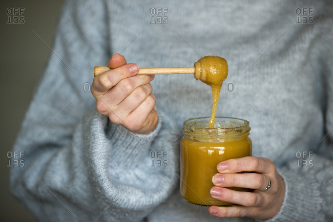 Hands of teenage girl holding honey jar and honey dipper- close-up