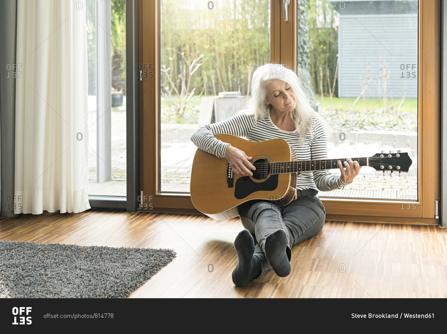 Mature woman sitting on the floor of living room playing guitar