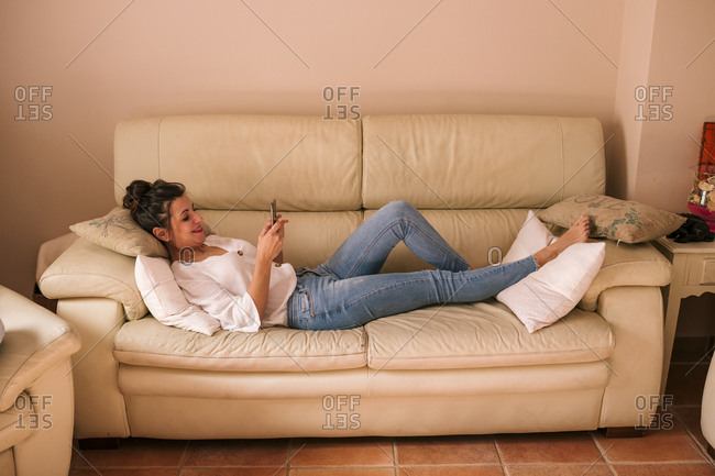 gebouw koppeling Rust uit Woman lying on the sofa looking at the phone stock photo - OFFSET