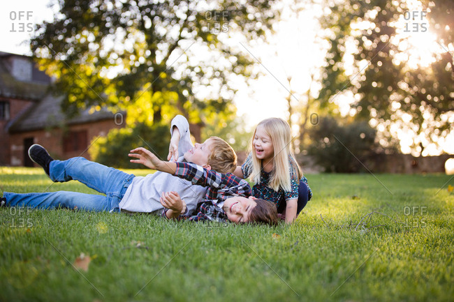 Siblings laughing and roughhousing outside in grassy field