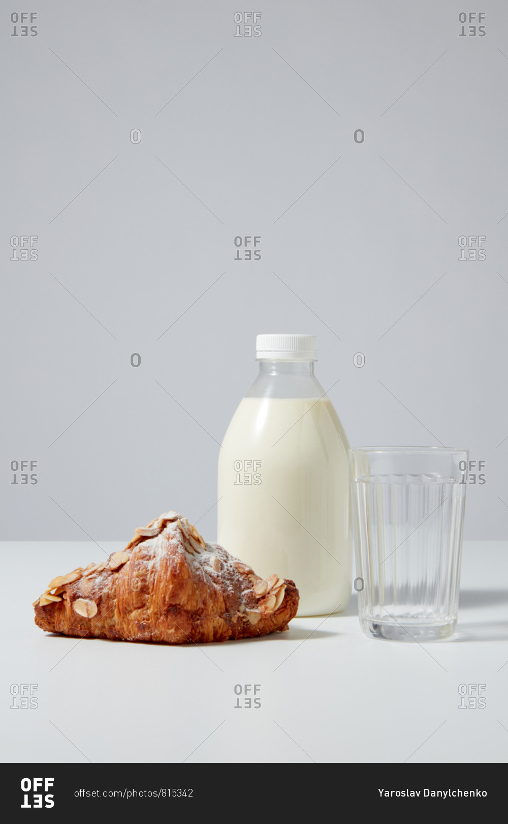 Bottle of organic milk with freshly baked homemade croissant covered in powdered sugar and almond chips on a light gray background. Place for text.