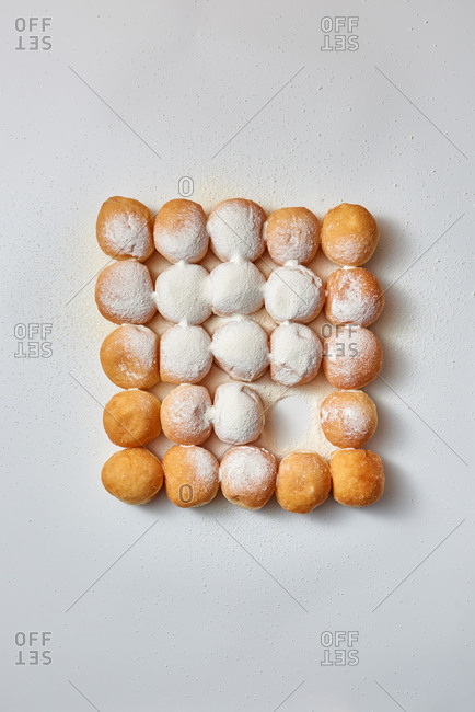 Homemade freshly baked delicious donuts in powdered sugar in a square pattern on a light gray background with copy space. Flat lay. Concept energy dessert.