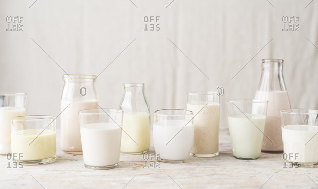 Flavored, pastel-colored alternative milks in glasses, bottles and pitchers