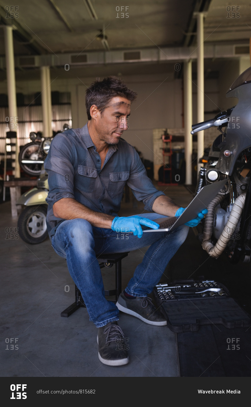 Side view of Caucasian bike mechanic wearing gloves while using laptop while working in garage