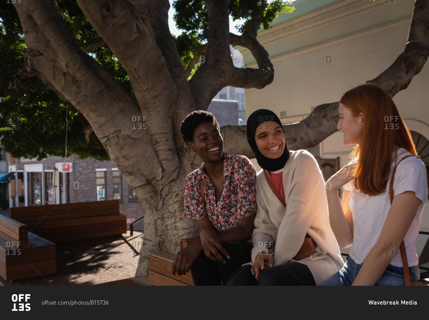 Side view of happy mixed race female friends interacting with each other while sitting under the tree