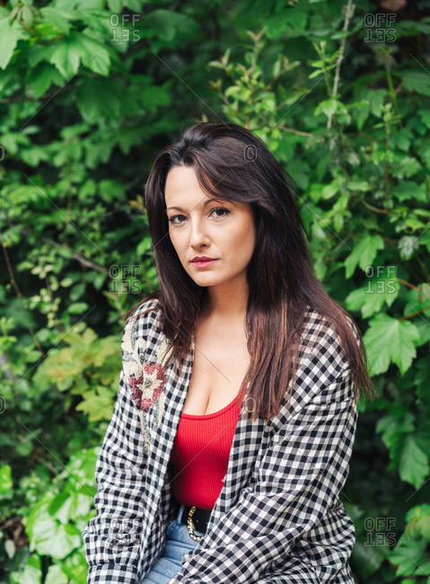 Young Brunette Woman Standing On The Park With Red And Plaid Clothes.