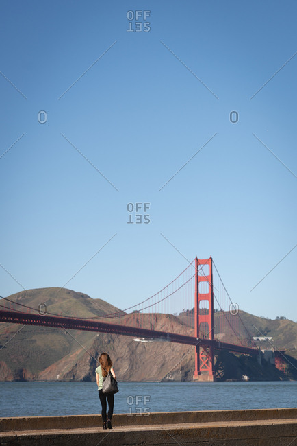 Rear view of beautiful woman walking from sitting wall near golden gate bridge