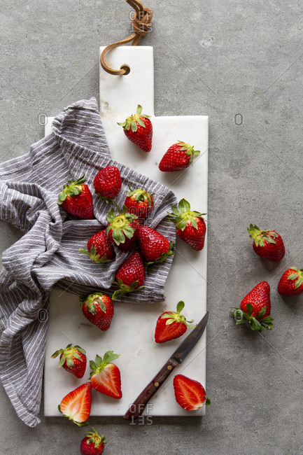 Fresh strawberries in striped kitchen towel on white marble board over grey concrete background