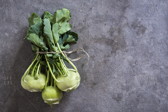 Bundle of fresh kohlrabi stems with leafs over grey concrete background