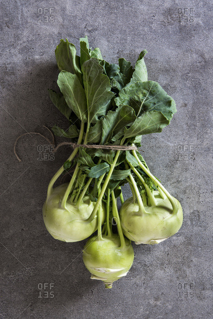 Bundle of fresh kohlrabi stems with leafs over grey concrete background