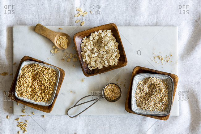 Oat grains, rolled oats and oat grist in wooden bowls on white marble board over white background