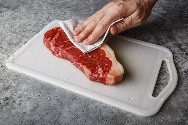 Raw fresh meat Steak Strip loin on cutting board drying up excess moisture by Male hand with paper towel