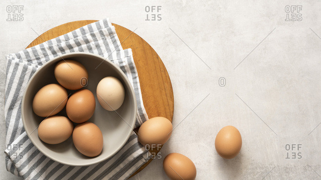 Brown and white eggs in a bowl on a textured grey background with copyspace.