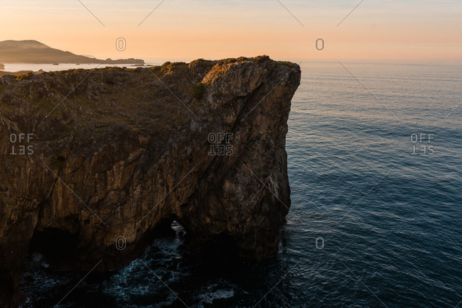 Panoramic view of huge rocky cliffs above rippled water against sunset sky, Asturias, Spain