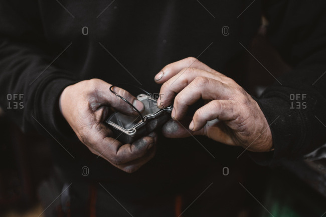 Unrecognizable repairman with dirty hands gluing broken part in workshop
