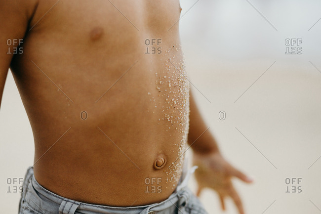 Unrecognizable African American child with sand on tummy spending time on beach