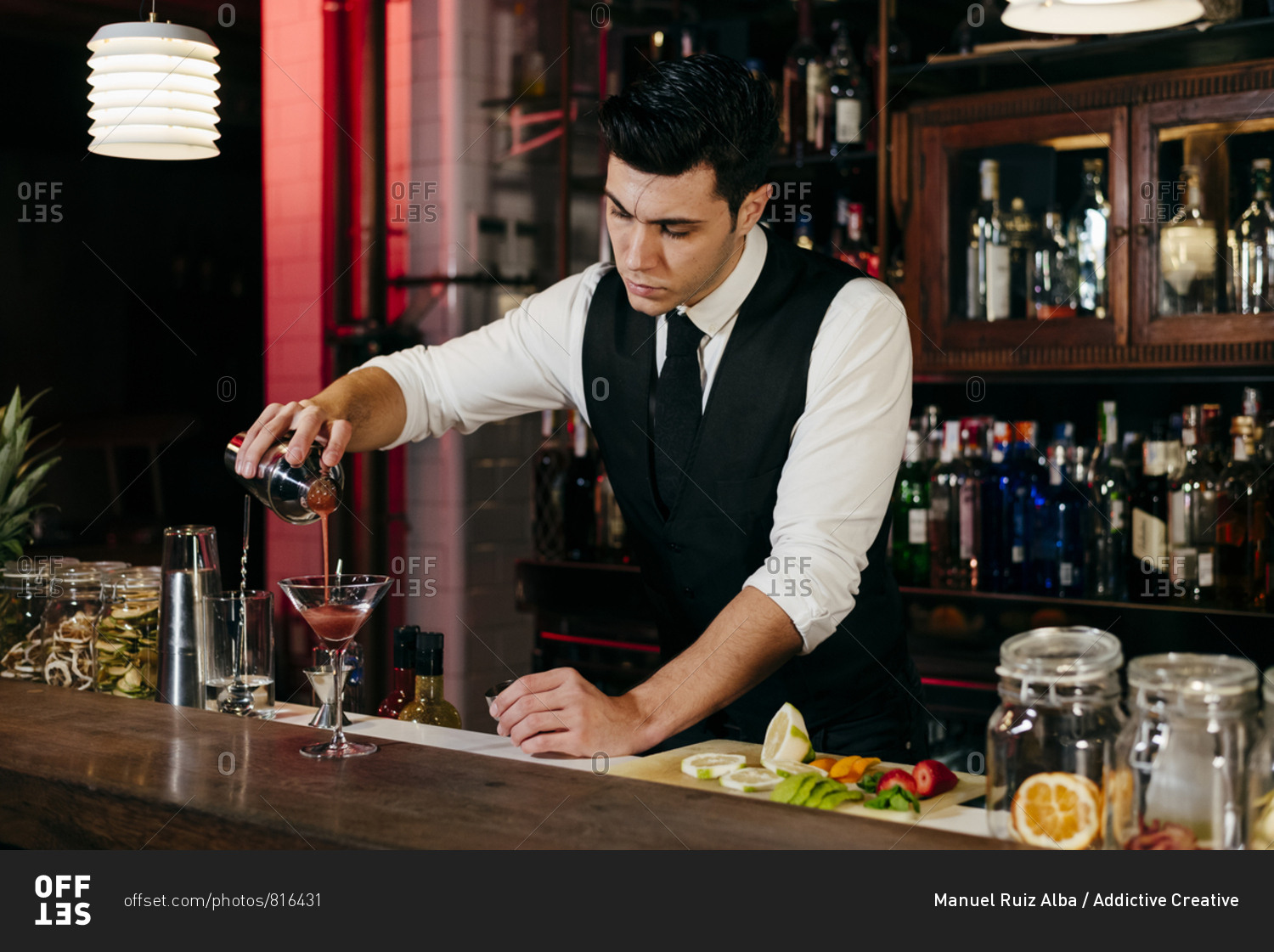 Young elegant barman working behind a bar counter pouring drink from