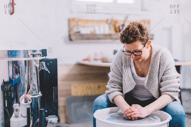 Female potter with dirty hands making clay pot on wheel in workshop