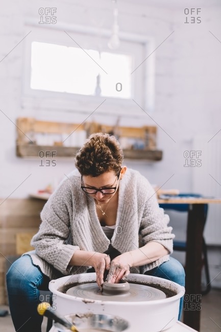 Female potter with dirty hands making clay pot on wheel in workshop