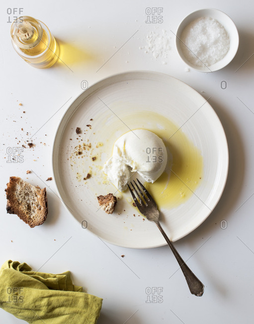 Plate with delicious fresh burrata placed on white tabletop near piece of bread and oil with salt