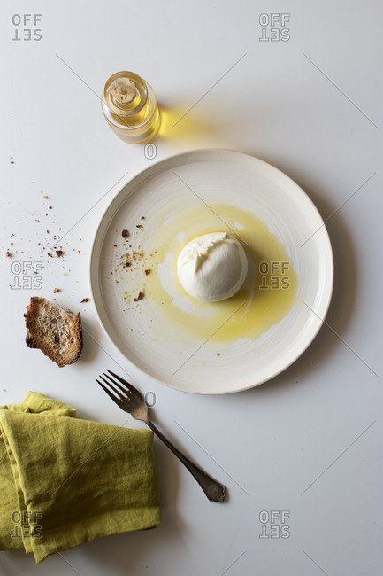 Plate with delicious fresh burrata placed on white tabletop near piece of bread and oil with salt