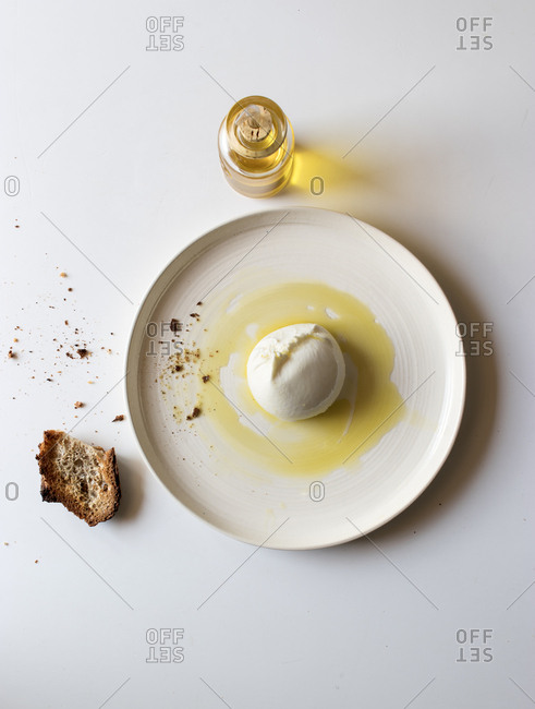 Plate with tasty burrata and piece of bread with oil on white background