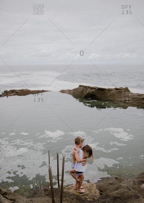 Siblings holding each other in a hug on the tide pool overlooking the ocean