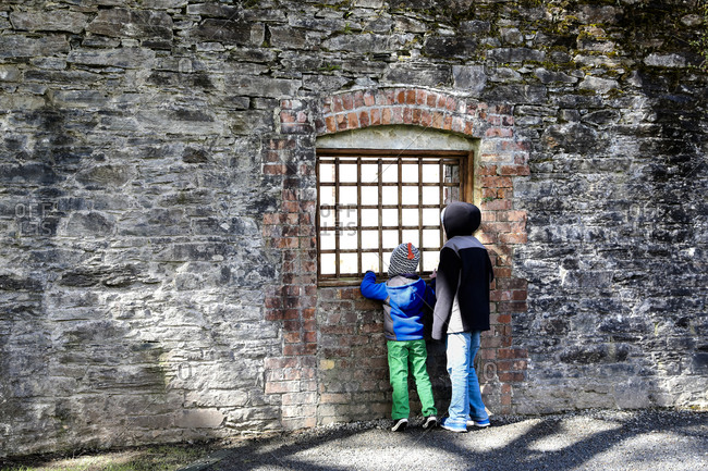 Tween Boy and Younger Brother Look Through Iron Window in Stone Wall