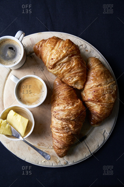Croissants on a round wooden board with butter and two espresso?s,