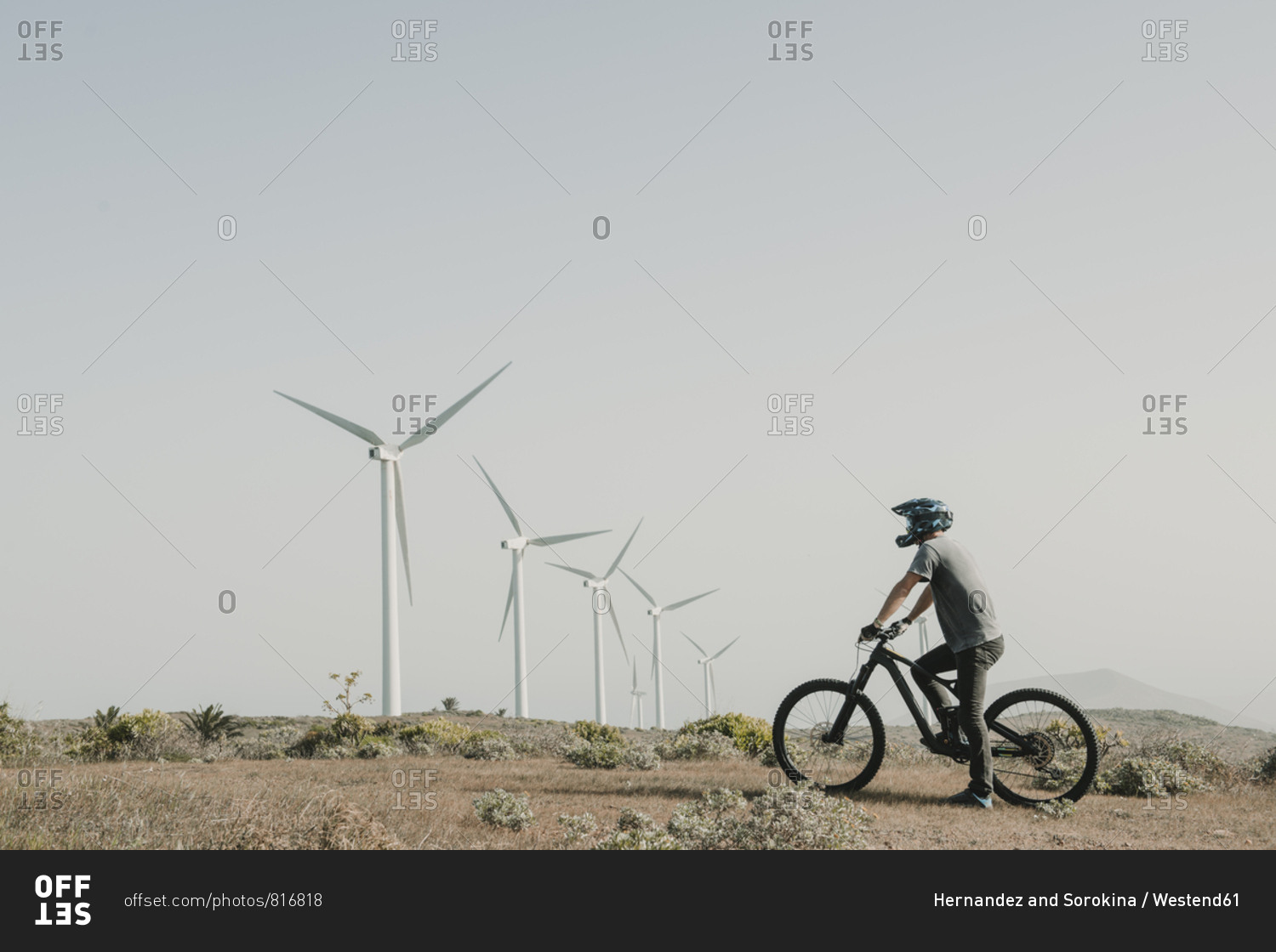 Spain- Lanzarote- mountain biker on a trip in deserted landscape with wind turbines in background