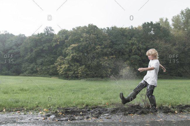 Boy splashing with dirty water of puddle