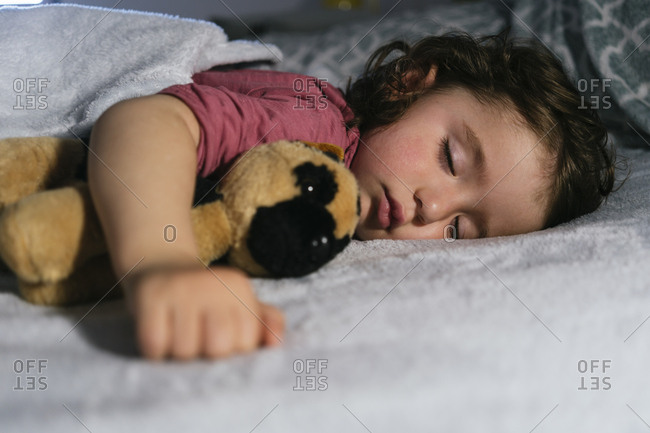 Portrait of toddler girl sleeping in bed  with a soft toy dog