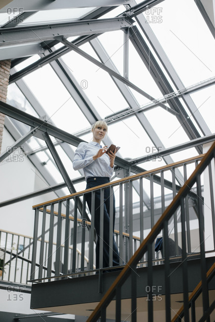Businesswoman standing in loft office- using smartphone