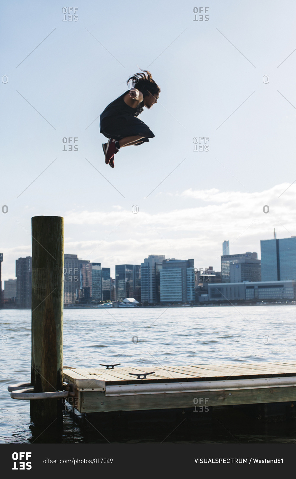 USA- New York- Brooklyn- young man doing Parkour jump from wooden pole in front of Manhattan skyline