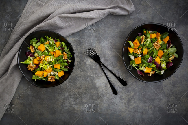 Two bowls of mixed green salad with hokkaido pumpkin and walnuts
