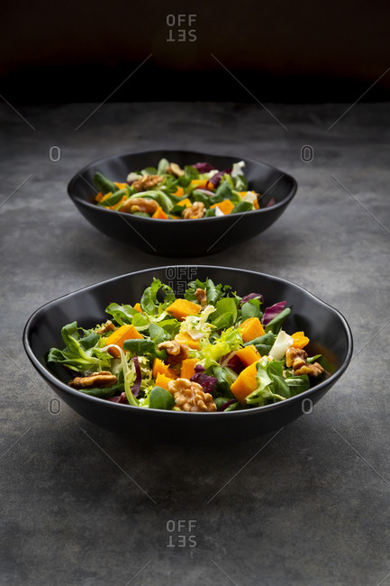 Two bowls of mixed green salad with hokkaido pumpkin and walnuts