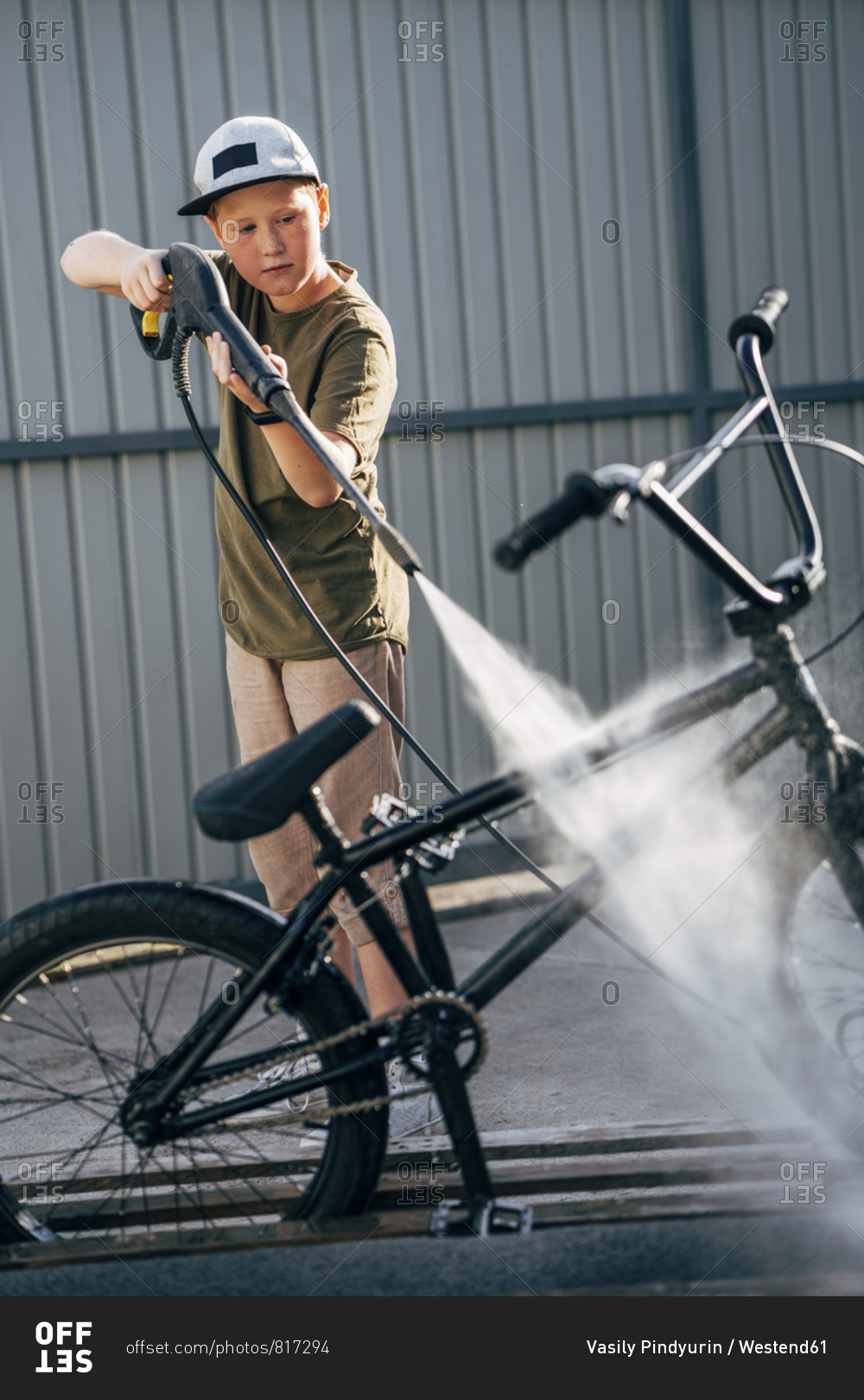 Boy washing bmx bike with pressure washer on yard