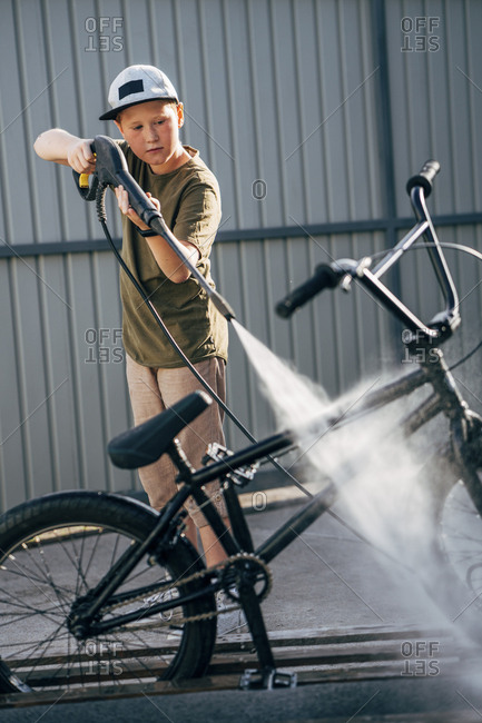 Boy washing bmx bike with pressure washer on yard