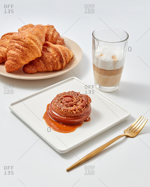 Cinnamon sweet bun with caramel and nuts, croissants and coffee drink in a glass around a white background. Sweet snack