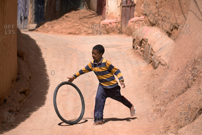 Ait Benhaddou, Morocco - April 12, 2019: Unidentified young boy plays with old tire along a dirt road in the city