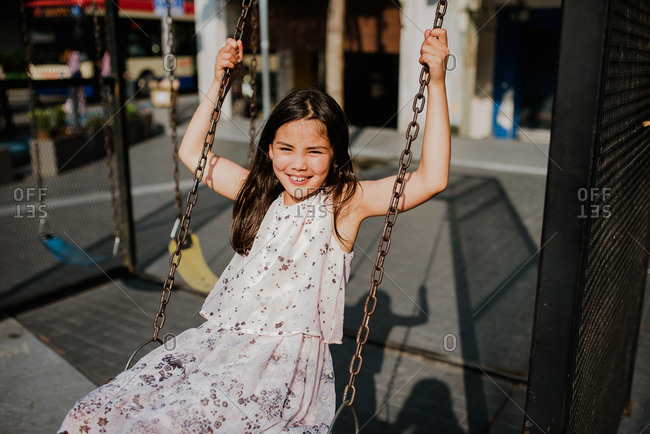 Adorable girl swinging on a swing set in a commercial district with bright afternoon light
