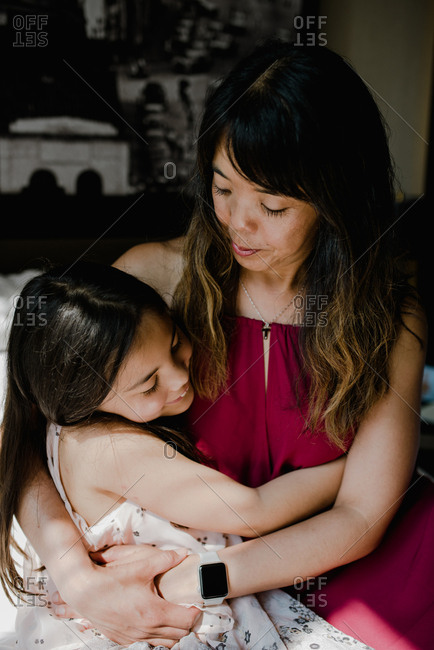 Asian mother and daughter hugging at home in dappled sunlight