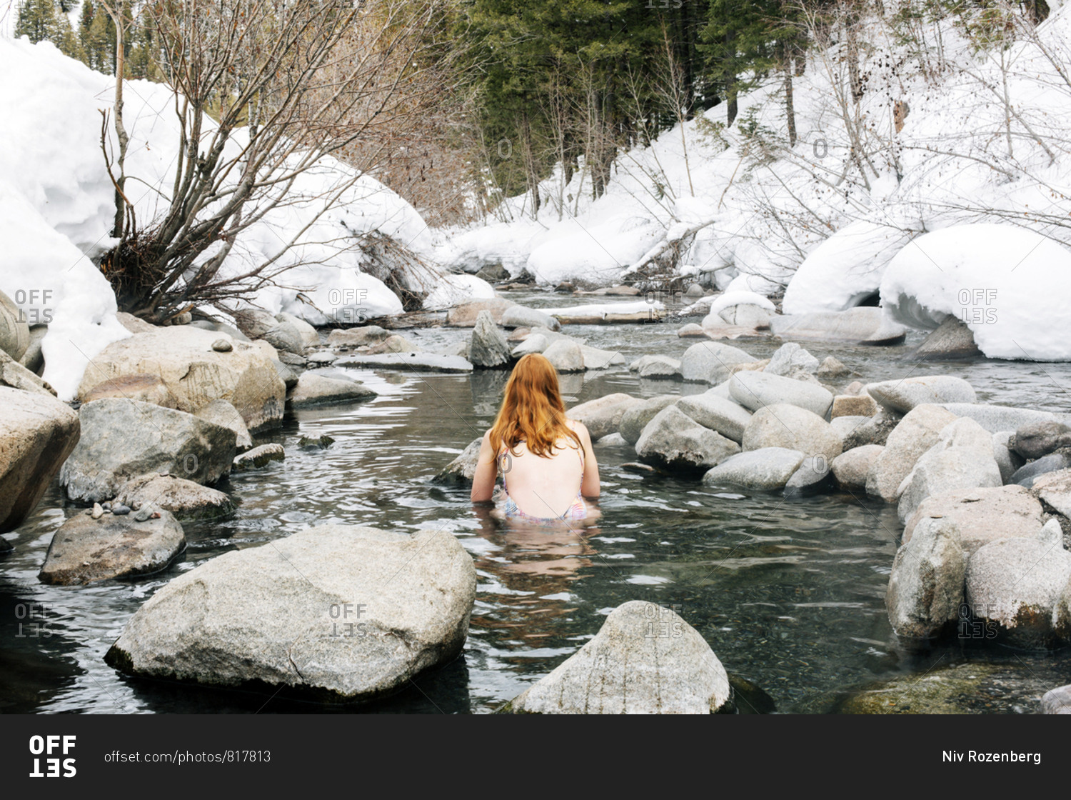 Redhead woman enjoying a hot spring by snowy river in Sun Valley, Idaho
