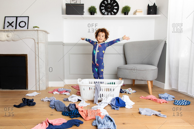 Playful boy in pajamas making mess with laundry basket
