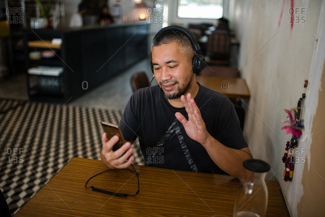 Man video chatting on phone at cafe while wearing headphones