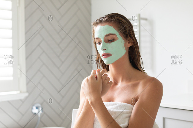 Close-up of thoughtful woman with facial mask sitting in the bathroom