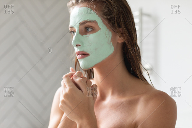 Close-up of thoughtful woman with facial mask sitting in the bathroom