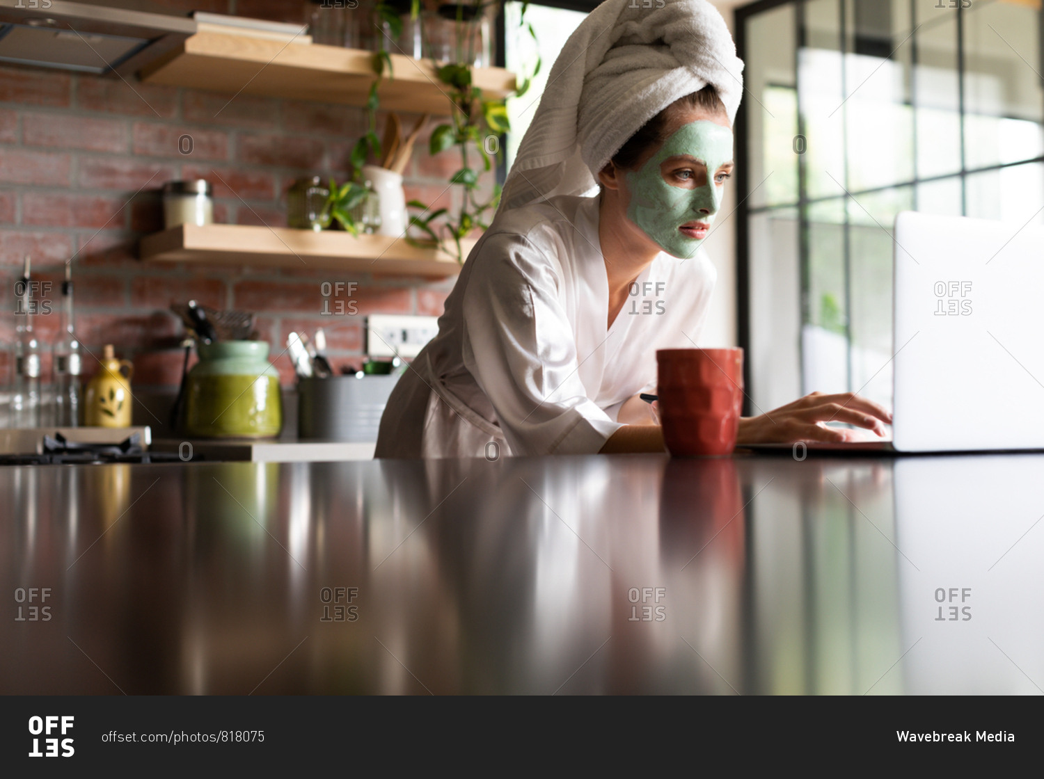 Beautiful woman in bathrobe using laptop on the kitchen counter at home